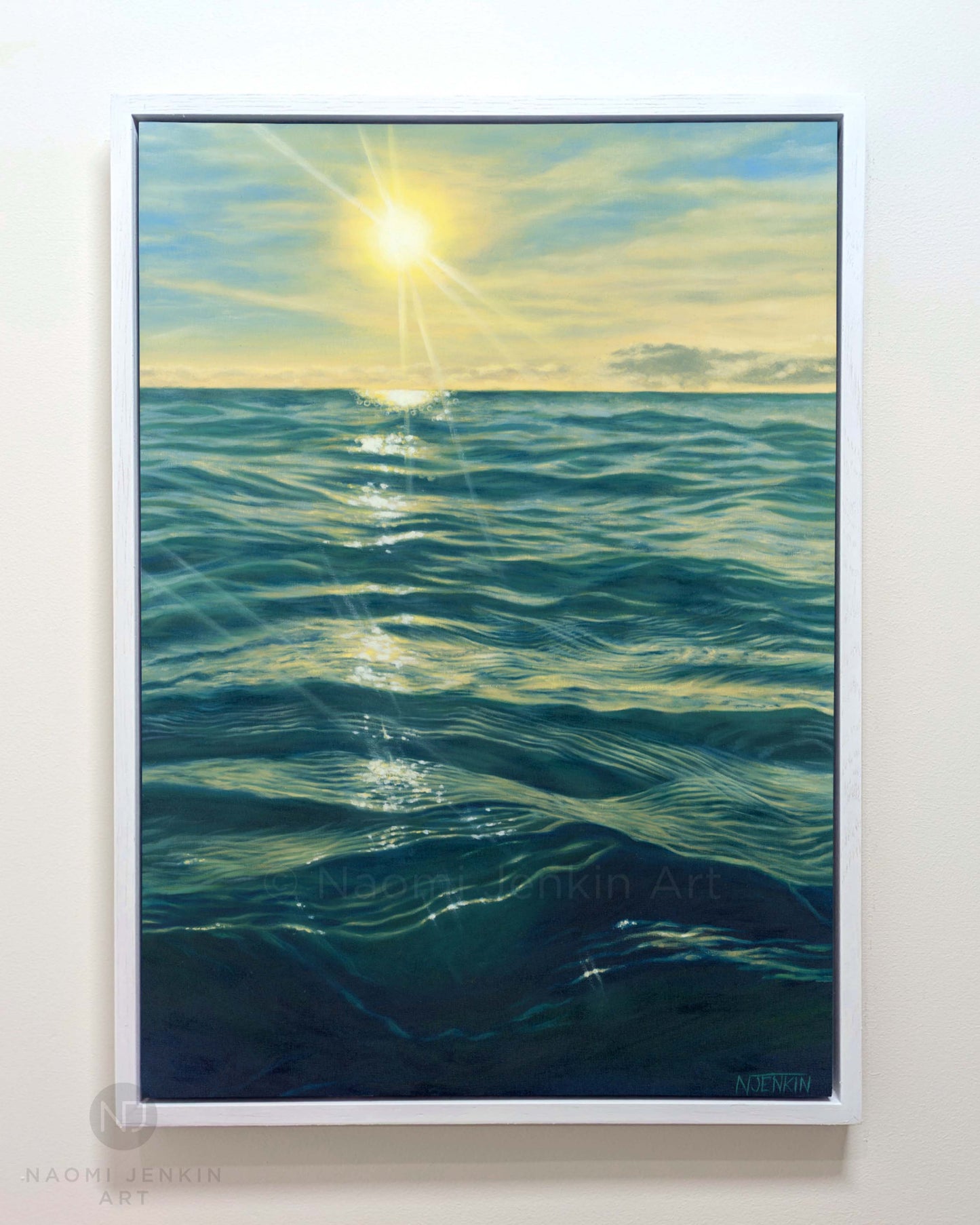 "Last Days Of Summer" - framed original oil painting of an ocean sunset by artist Naomi Jenkin, featuring deep blue-green waves reflecting a bright yellow sun and golden sky. Framed in a white frame.