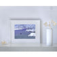Framed artwork by Naomi Jenkin of a snowy landscape with a bird on the ice displayed in a white frame. 