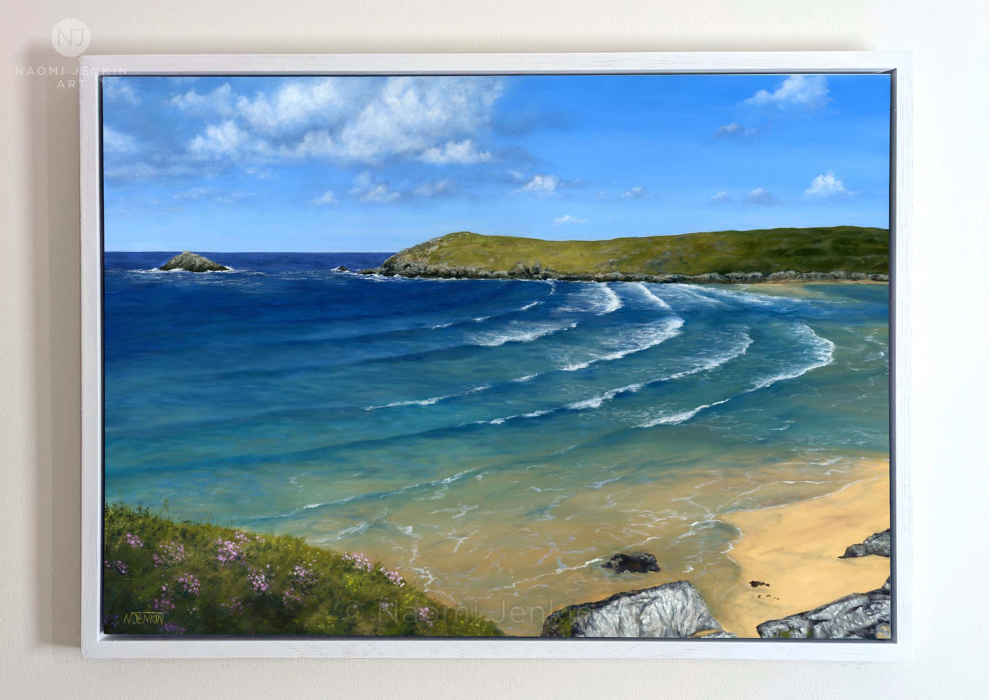 Framed original oil seascape painting by Naomi Jenkin of Crantock Bay, Cornwall in summer, showing turquoise sea with swell curving into the bay at high tide, sea pinks flowering in the foreground, and Pentire Headland and Goose Rock in the distance