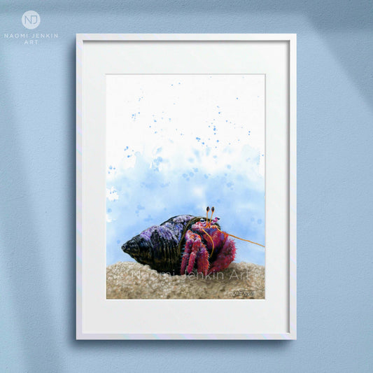 Framed artwork of a colourful hermit crab on sand with a blue watercolor background, displayed on a light blue wall. Artist - Naomi Jenkin. 