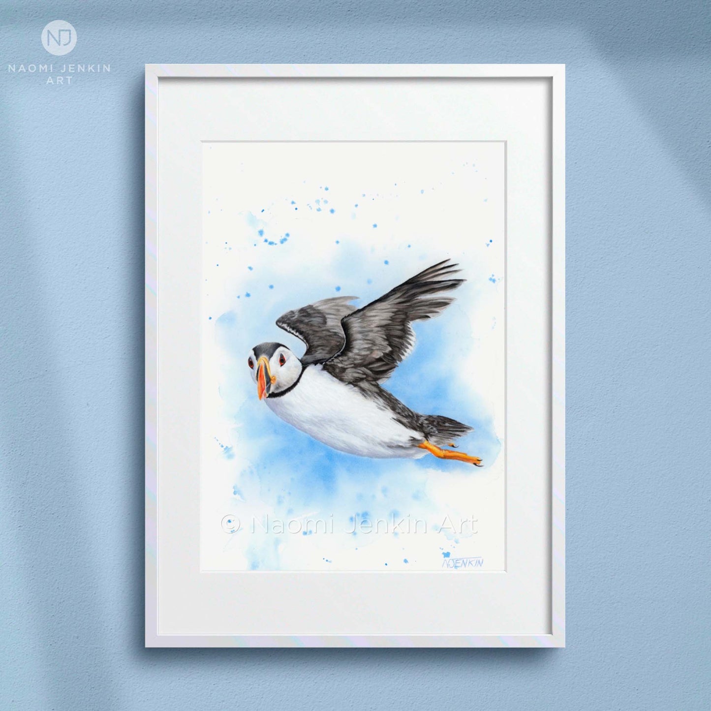 Framed art print of a puffin in flight on a light blue background by artist Naomi Jenkin. 