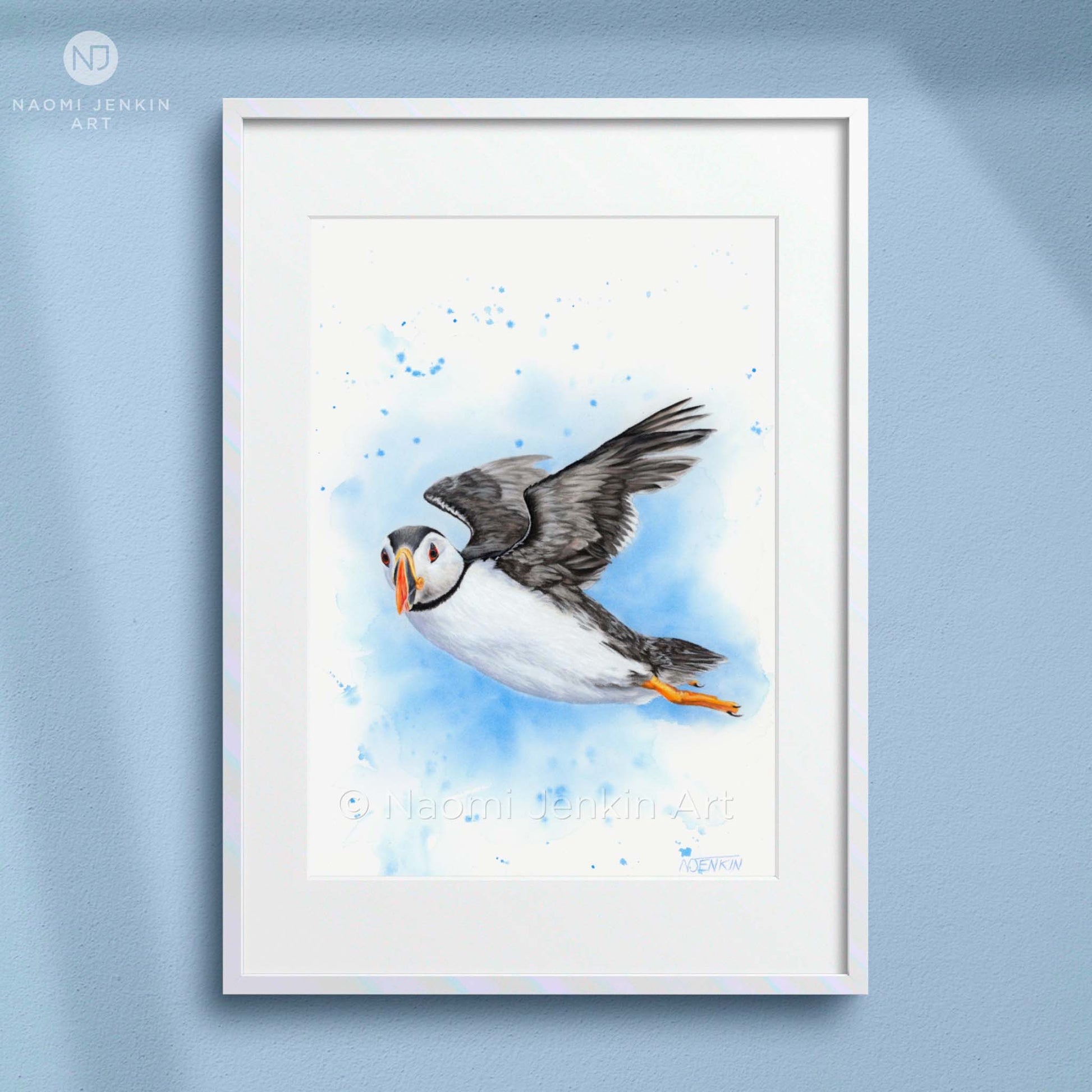 Framed art print of a puffin in flight on a light blue background by artist Naomi Jenkin. 